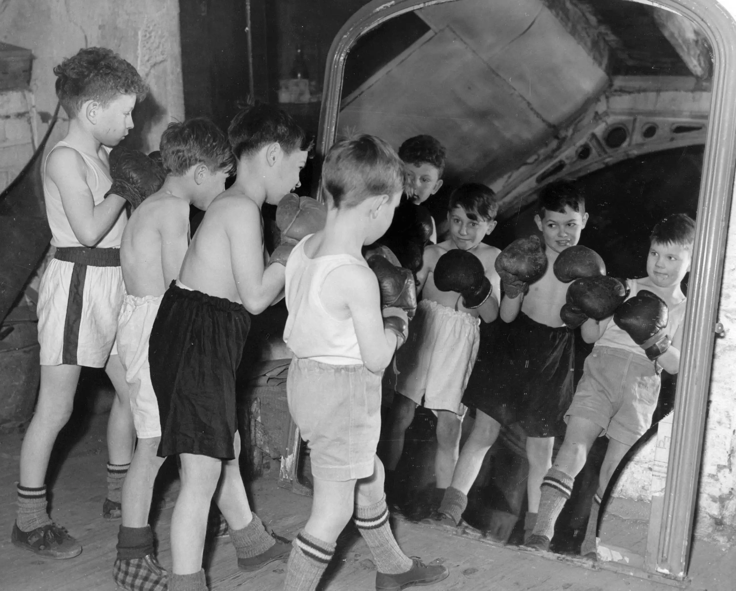 Black and white photo of young boys in boxing gloves lined up to spar