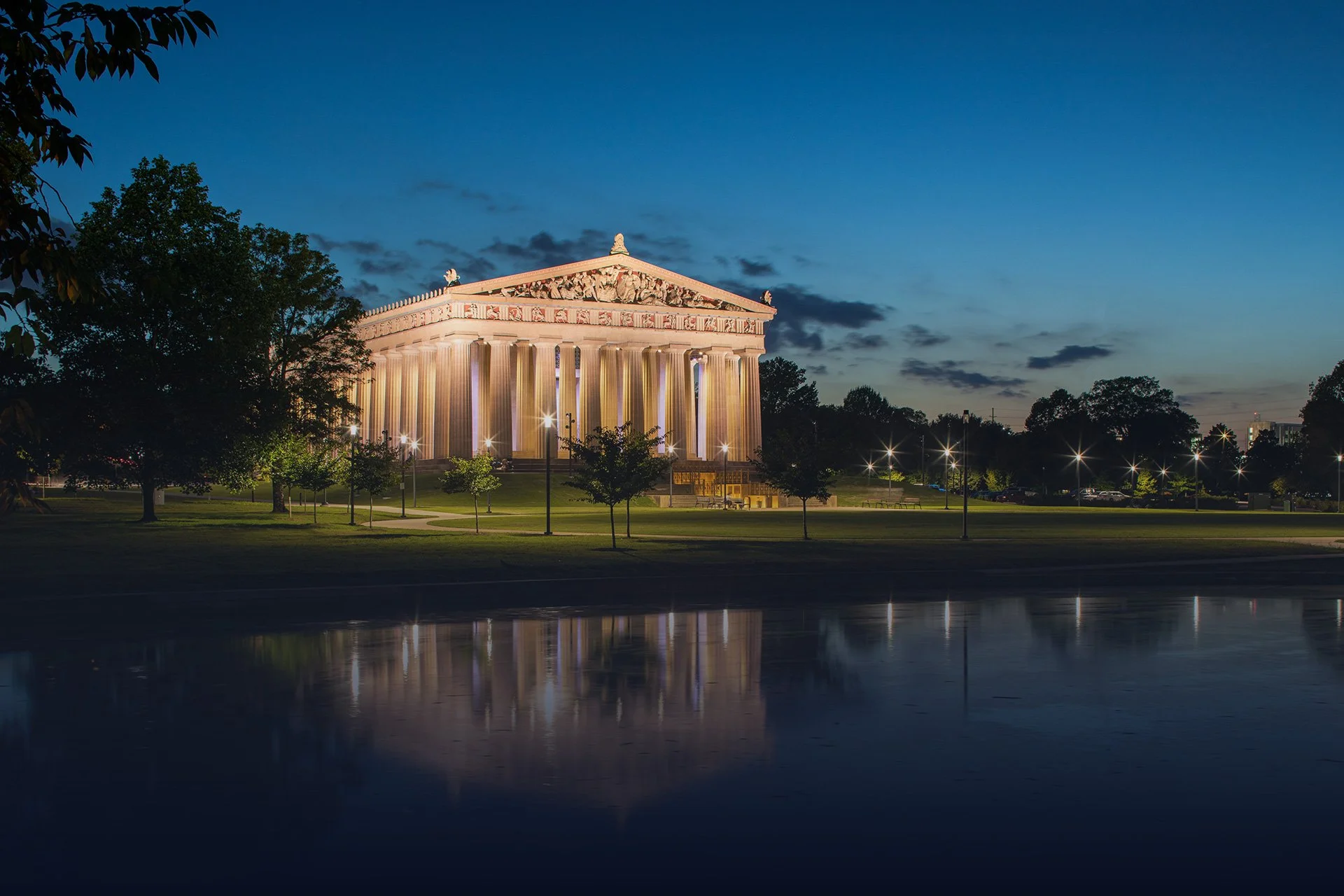 The Parthenon replica in Nashville's Centennial Park lit up at dusk and reflected in the lake