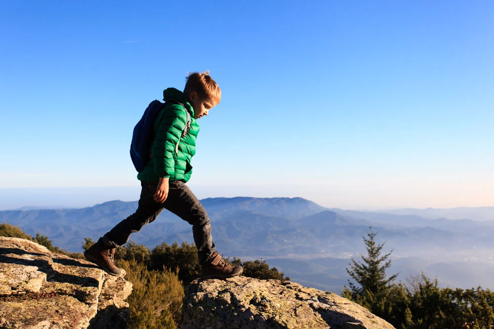 Young boy with a backpack stepping across rocks on a mountain overlook