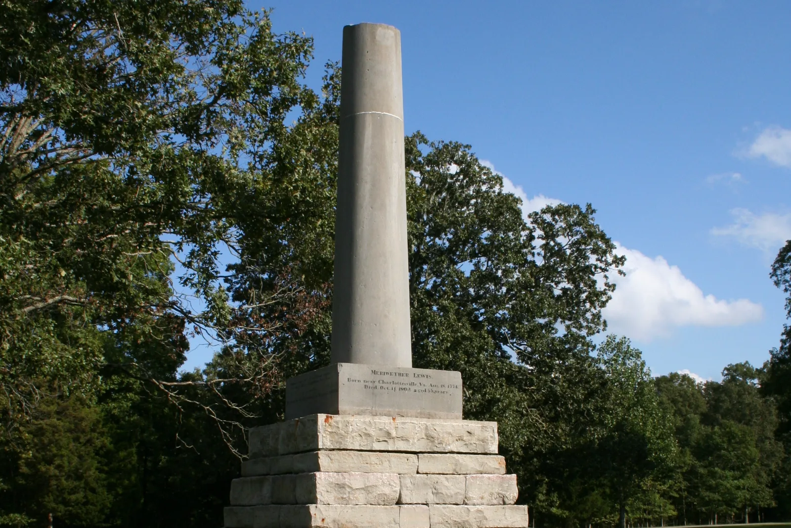 The broken stone column of the Meriwether Lewis Monument rising above its stepped limestone base among trees on the Natchez Trace